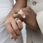 Up close shot of a wedding ring on a white female's hand and a wedding band on an Indian man's hand as the two newly weds hold hands and cross pinky fingers.